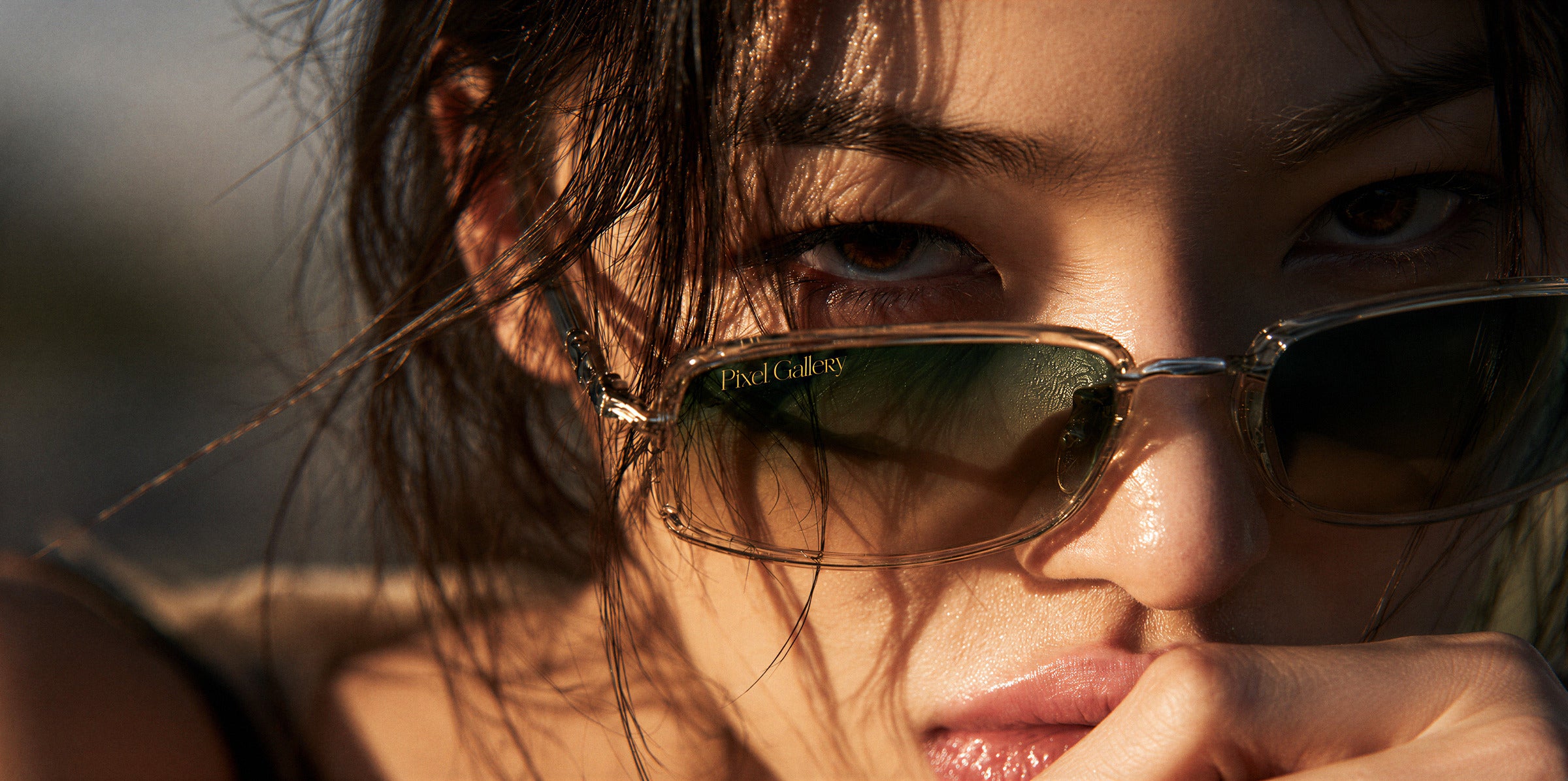 Close-up editorial portrait in gold-framed sunglasses at sunset, the Pixel Gallery name etched into the lens